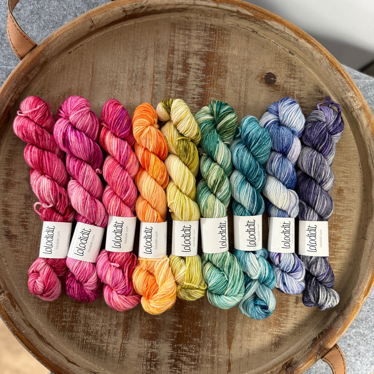 Colorful yarn skeins on a wooden tray with visible labels.